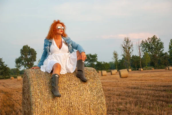 Roodharige vrouw poseren op het veld in de buurt van een stapel hooi — Stockfoto