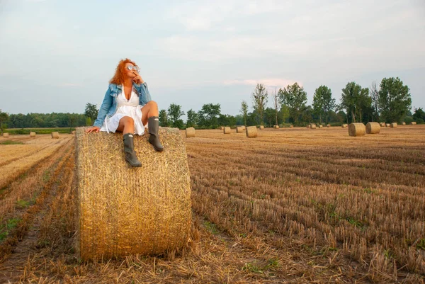 Roodharige vrouw poseren op het veld in de buurt van een stapel hooi — Stockfoto