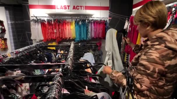 Jonge vrouw kleding in de kledingwinkel kiezen — Stockvideo