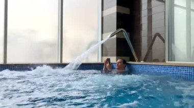 Havuzda akıllı telefon kullanan orta yaş adam