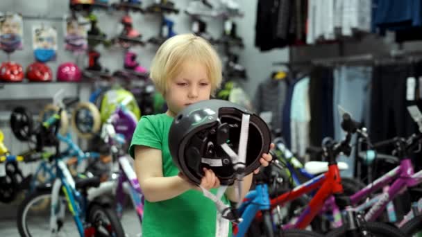 Menino escolhe capacete de bicicleta na loja — Vídeo de Stock