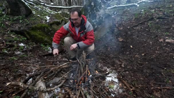 Medelålders man sitter vid elden i skogen — Stockvideo