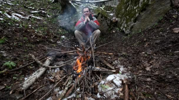 Middle-aged man sits by the fire in the forest — Stock Video