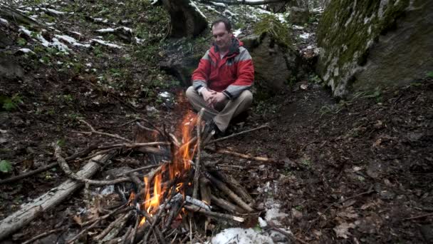 Hombre de mediana edad se sienta junto al fuego en el bosque — Vídeos de Stock