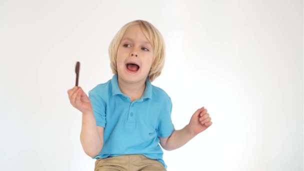 Menino comendo uma barra de chocolate em um fundo branco — Vídeo de Stock