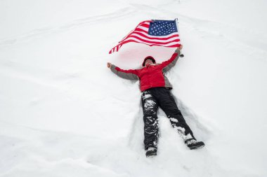 Amerikan bayrağını taşıyan bir adam karda yatıyor.