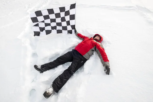 Чоловік лежить на снігу з фінішним прапором — стокове фото