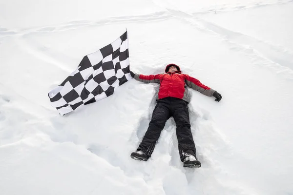 Чоловік лежить на снігу з фінішним прапором — стокове фото