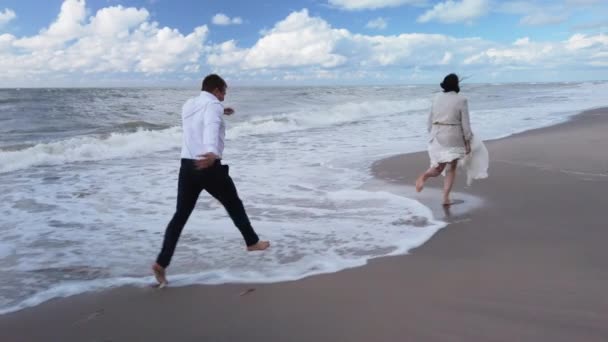 Счастливая молодожёны, прыгающие через морские волны — стоковое видео