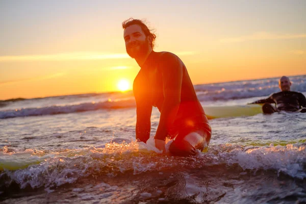 Sörfçü denizde sörf tahtasında oturuyor.