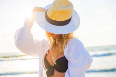 Bikini giyen ve plajda şapka takan mutlu bir kadın.
