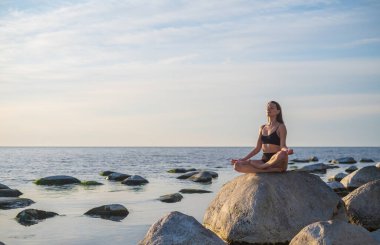 Genç bir kadın deniz kenarında meditasyon yapıyor.