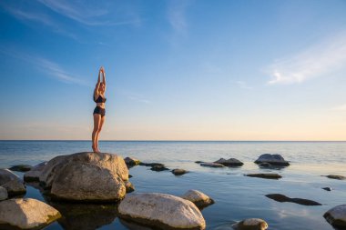 Dağ pozunda deniz kıyısında duran kadın.