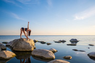 Devrimci Üçgen pozunda denizin yanında duran kadın.
