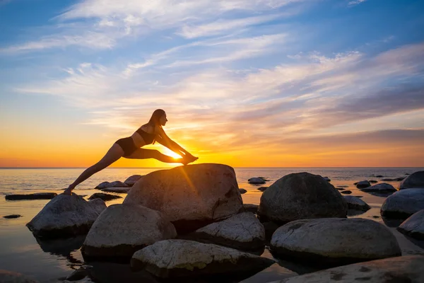 Ung kvinna gör sprickor på stenar under solnedgången — Stockfoto