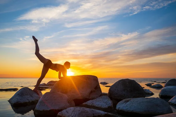 Slim fêmea fazendo ioga contra o céu brilhante pôr do sol — Fotografia de Stock