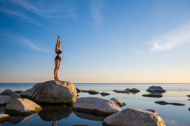 Dağ pozunda deniz kıyısında duran kadın.