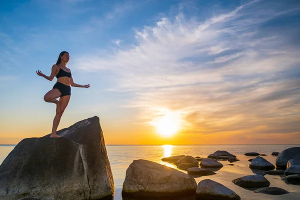 Woman meditating on stone in Tree pose