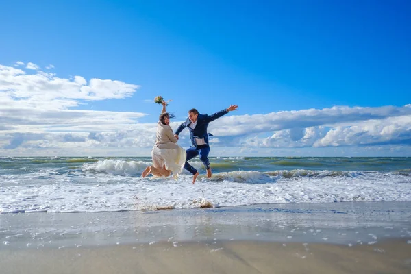 Невеста и жених прыгают возле морских волн — стоковое фото