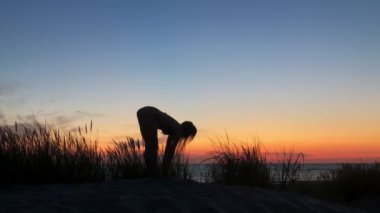 Akşamları deniz kıyısında yoga yapan tanınmayan bir kadın.