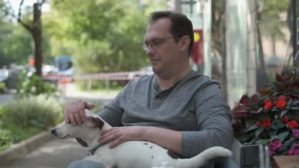 Зрелый мужчина гладит собаку в уличном кафе — стоковое видео