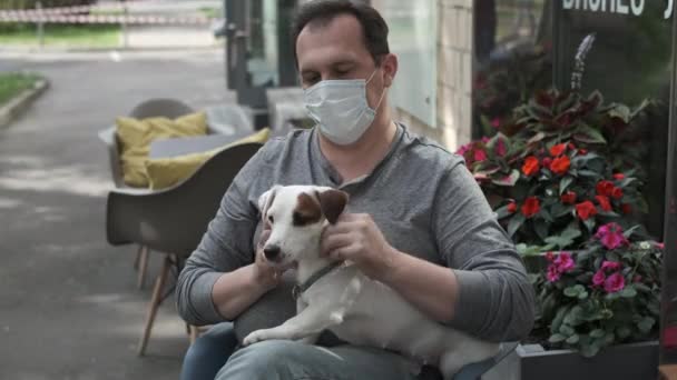 Sokak kafesinde maskeli bir adam köpeğini okşuyor. — Stok video
