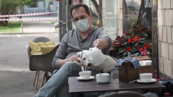 Sokak kafesinde maskeli bir adam köpeğini okşuyor. — Stok video