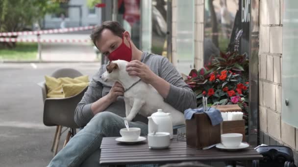 Hombre con máscara acariciando perro en la cafetería de la calle — Vídeos de Stock