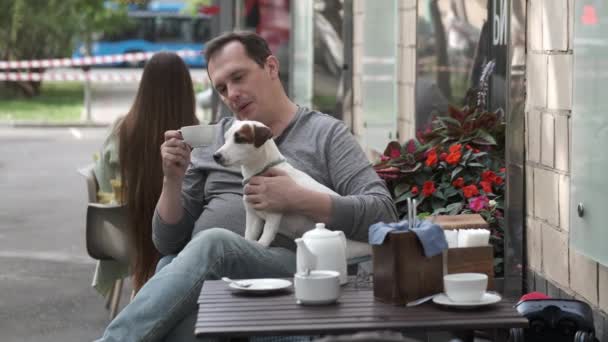 रस्त्यावर कॅफेमध्ये मास्कमध्ये माणूस काळजी घेणारा कुत्रा — स्टॉक व्हिडिओ