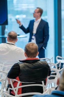 Katılımcılar otururken ve odaklanırken, bir konuşmacı modern bir mekandaki bir iş seminerinde sunum yapıyor..