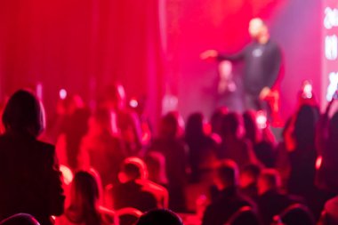 Bir olay sırasında sahnede sunucuyu ya da sanatçıyı izleyen bulanık kırmızı ışıklı seyirci.