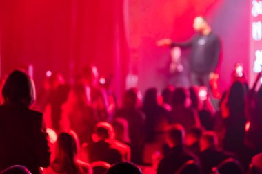 Bir olay sırasında sahnede sunucuyu ya da sanatçıyı izleyen bulanık kırmızı ışıklı seyirci.