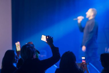 Konser kalabalığı ışıkların altında cep telefonlarıyla sahnede canlı bir performans yakalıyor.
