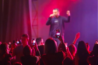 Canlı konsere katılan izleyiciler, akıllı telefonlarla performansı yakalamak, müzik ve eğlencenin tadını çıkarmak. Canlı sahne ışıklandırması gösteri sırasında heyecan verici atmosfer yaratır.