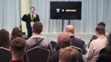 Sunucu, eğitime odaklanan bir konferans ortamında izleyicilere konuları tartışır.