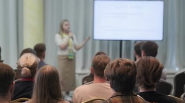 Bir konferans ortamında izleyicilere sunum yapan konuşmacı, katılım ve bilgi paylaşımını teşvik ediyor.