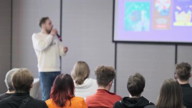 Erkek sunucu bir gruba sesleniyor, görsel slaytlar sergiliyor, öğrenme ve bağlanmayı teşvik ediyor