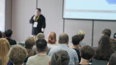 Konferans odasında bir konuşmacının sunumunu dinleyen büyük bir grup insan. Etkinlik boyunca eğitim, ağ ve bilgi paylaşımına vurgu.