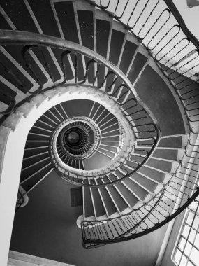 Siyah ve beyaz sarmal merdivenler iç uzayda aşağı doğru kıvrılarak kıvrımları ve mimari ayrıntıları gösteriyor.