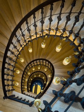Süslü demir korkuluklu ve sıcak kolye lambalı sarmal merdiven, tarihi iç mekanlarda yukarıdan görüldü.