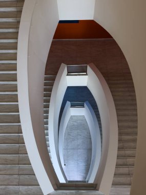 Beyaz raylı çift kıvrımlı merdivenlerin çarpıcı görüntüsü ve mermer basamaklar sanatsal bir girdap oluşturuyor. Modern iç tasarım geometri ve uzayı vurguluyor