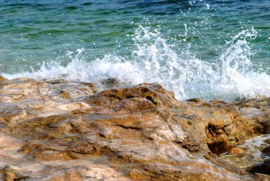 Deniz dalgaları kayalara çarpıyor, püskürtüyor.