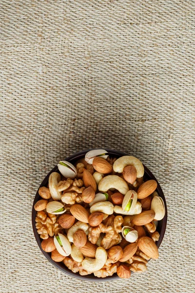 Mix of nuts of nut of nut of cashew, almonds, pistachios, hazelnuts and walnuts in a wooden cup against the background from burlap fabric. Nuts as structure and background, macro. Top view. It vertically