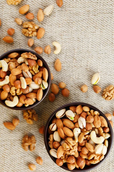 A mixture of cashew nuts, almond nuts, pistachios, hazelnuts and walnuts in a wooden cup against the background of burlap fabric. Nuts as structure and background, macro. Two cups of nuts.