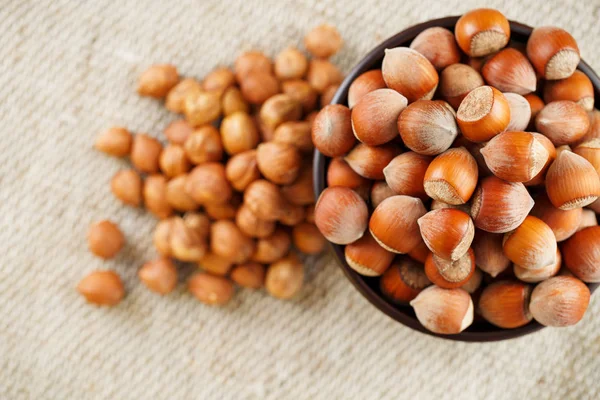 Peeled hazelnuts in a wooden, dark brown cup on a burlap cloth. Super Food, Raw. View from above.