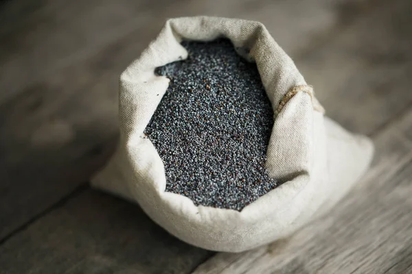 Poppy seeds in a burlap bag on a vintage wooden gray background. In country style. The tasty and useful seeds rich with protein and oils. It is poured out of a bag. Calcium content leader
