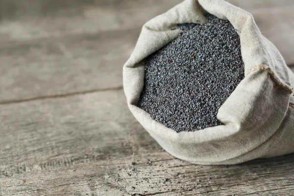 Poppy seeds in a burlap bag on a vintage wooden gray background. In country style. The tasty and useful seeds rich with protein and oils. It is poured out of a bag. Calcium content leader