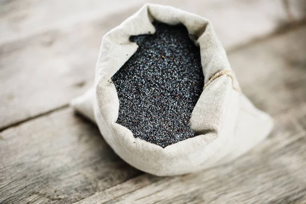 Poppy seeds in a burlap bag on a vintage wooden gray background. The tasty and useful seeds rich with protein and oils.