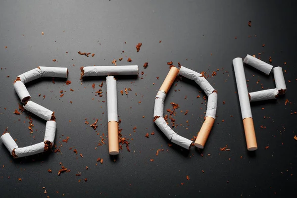 The inscription STOP from cigarettes on a black background. Stop smoking. The concept of smoking kills. Motivation inscription to quit smoking, unhealthy habit.