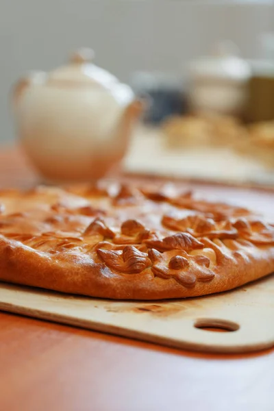 Russian pie with potatoes and mushrooms on the table. Freshly baked big cake decorated with flowers of their dough